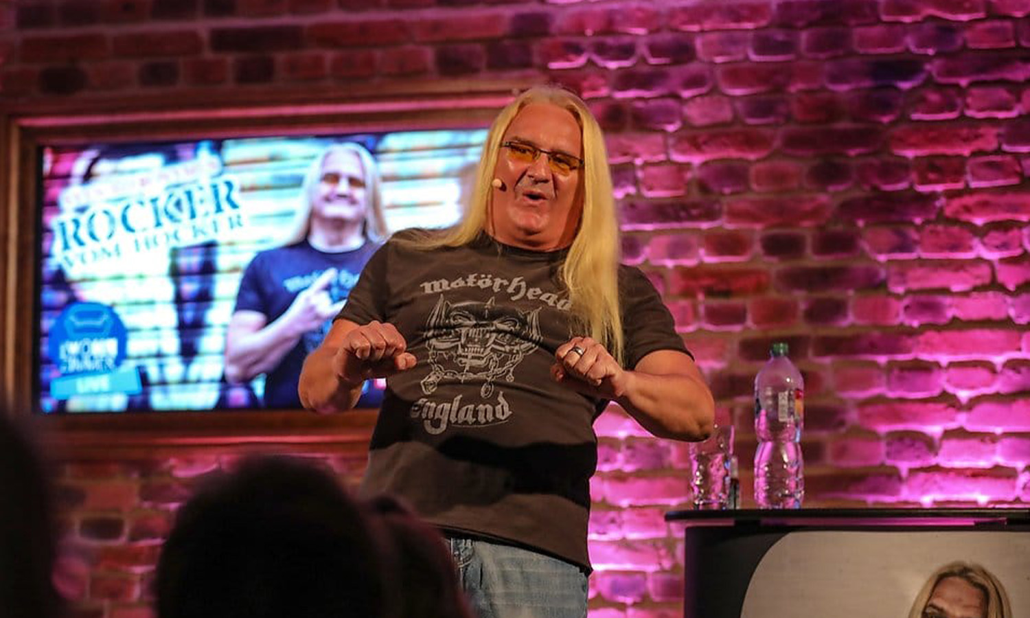 Comedian Sven Hieronymus steht mit Mikrofon auf der kleinen Bühne im RPR1. Wohnzimmer vor begeistertem Publikum.