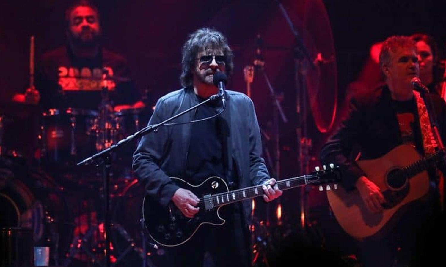 Jeff Lynne steht mit seiner Gitarre live auf der großen Bühne in der SAP Arena Mannheim vor begeistertem Publikum.