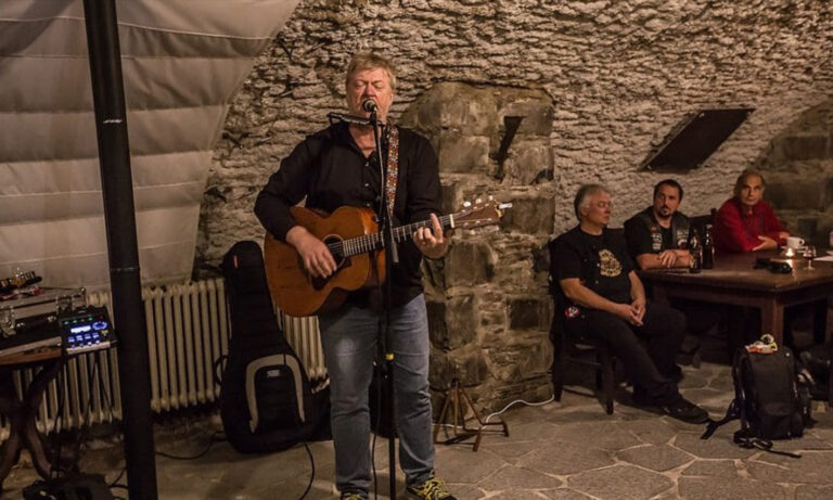 Musiker Paddy Schmidt steht mit seiner Gitarre live im historischen Burggewölbe auf der Burg Greifenstein vor Publikum.