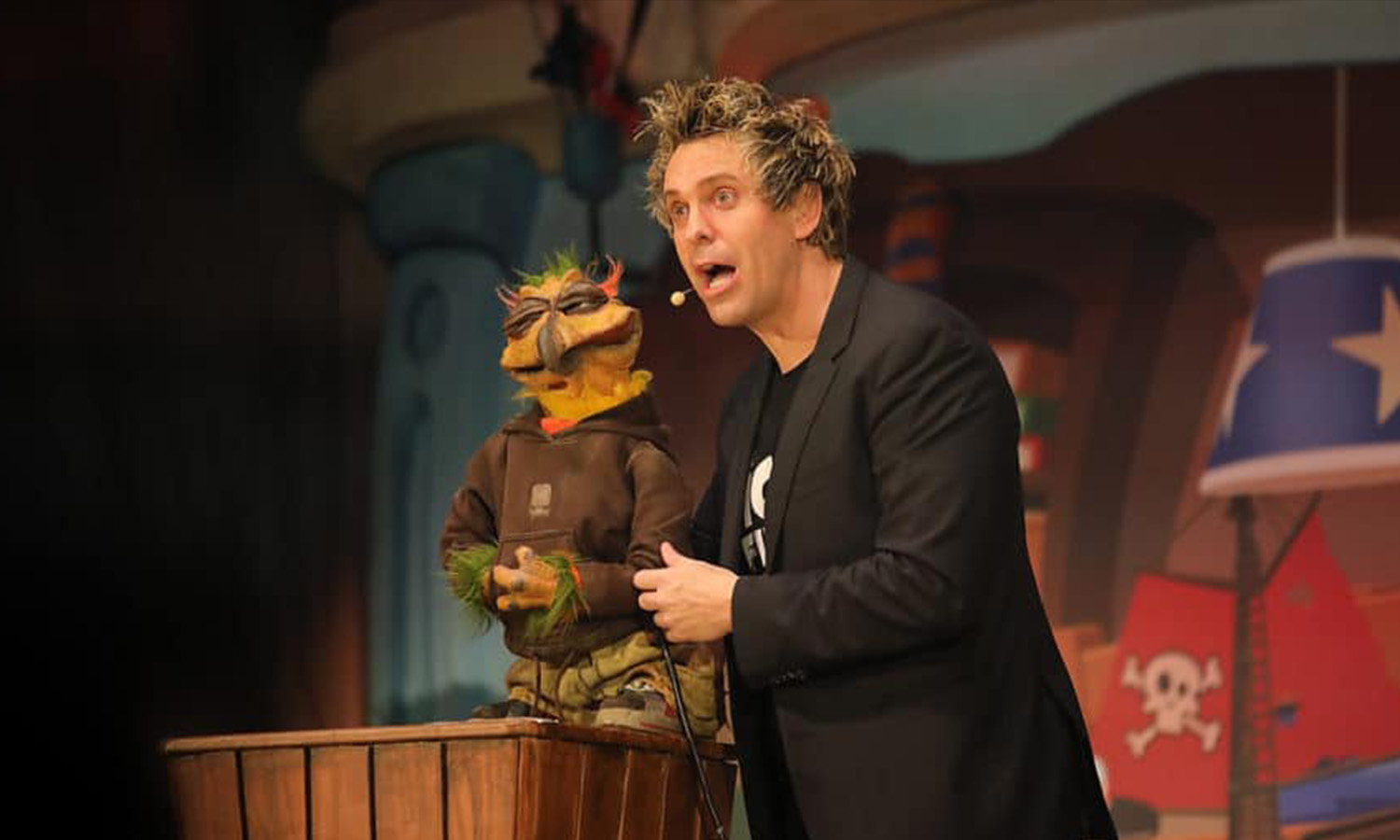 Puppet-Comedian Sascha Grammel steht mit einer seiner bekannten Puppen auf der Bühne im Mannheimer Rosengarten und lächelt ins Publikum.