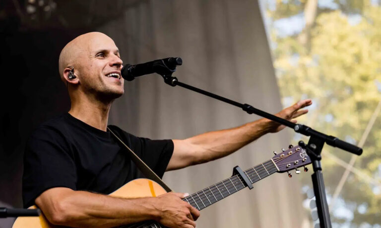 Milow steht mit seiner Akustikgitarre auf der Bühne des Rheingau Musik Festivals und singt ins Mikrofon, während im Hintergrund das stimmungsvolle Ambiente und das begeisterte Publikum zu sehen sind.